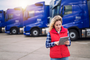 Woman checking on cargo insurance coverage before leaving with trucks behind her
